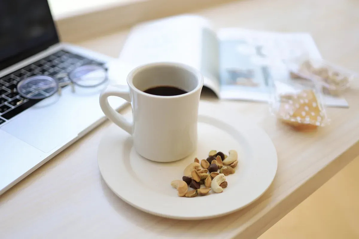 ノートパソコンの前にコーヒーカップやスナックミーのお菓子が置かれた様子