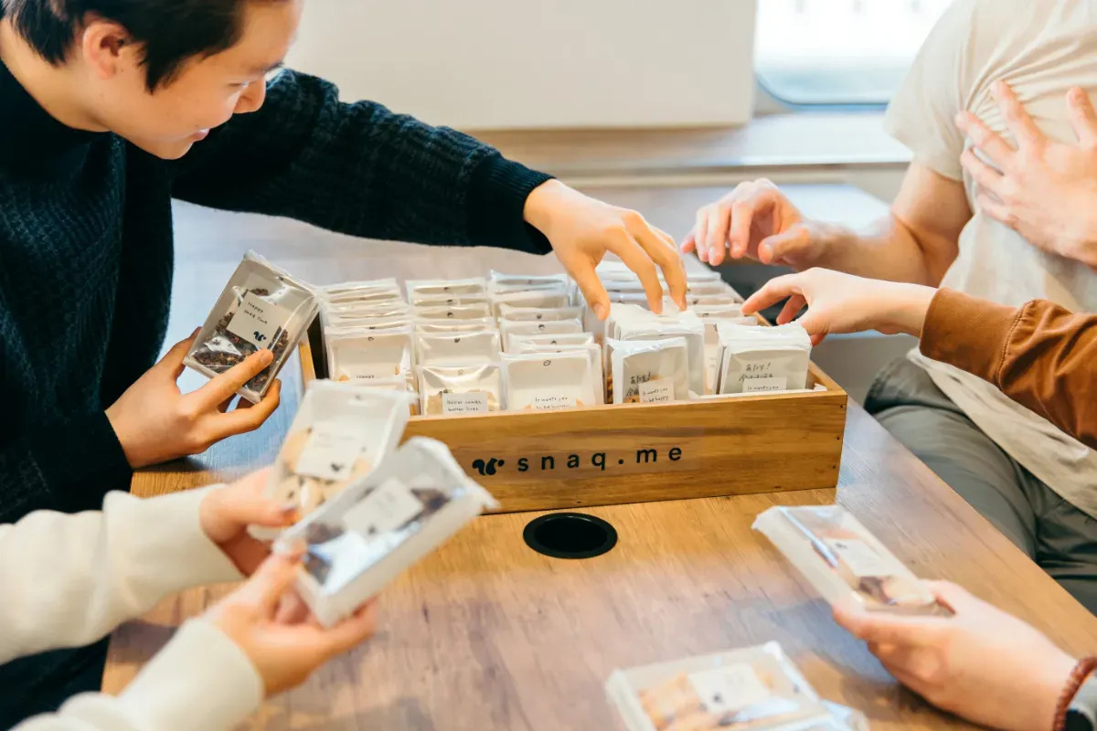 スナックミーオフィスの置き菓子什器を囲み、パッケージを手に取る従業員