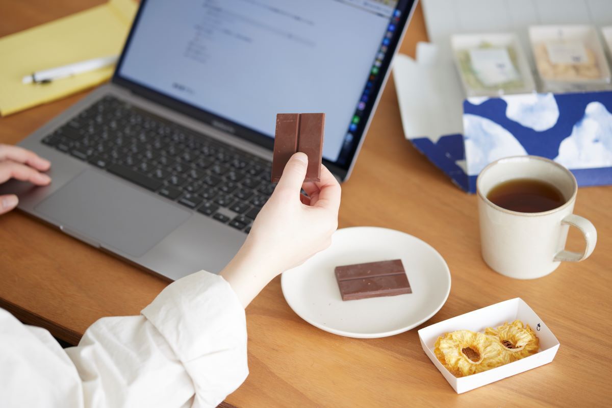 ノートパソコンで仕事をしながらスナックミーオフィスのお菓子を食べる従業員